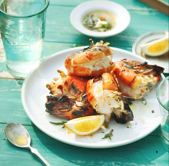 Gegrillte ganze Garnelen auf einem Teller, daneben Zitronen und eine Schüssel Marinade