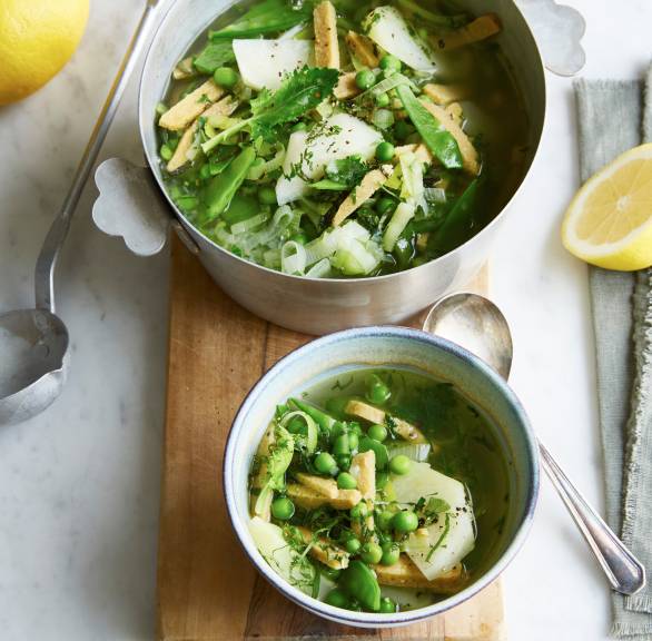 Grüne, vegane Minestrone mit Lupinenfilet in einem Topf und einer Suppenschale auf einem Tisch