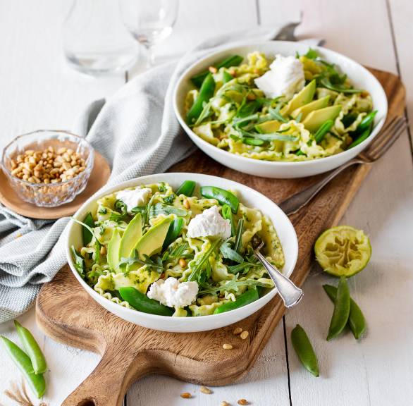 Mafaldine-Salat mit Basilikumpesto-Dressing auf zwei Tellern getoppt von Avcoadostücken, Mascarponeklecksen und Pinienkernen