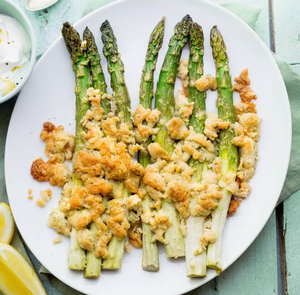 Grüner Spargel aus dem Ofen in ganzen Stangen auf einem Teller getoppt mit Parmesanstreuseln, daneben Joghurtdip in einer Schale
