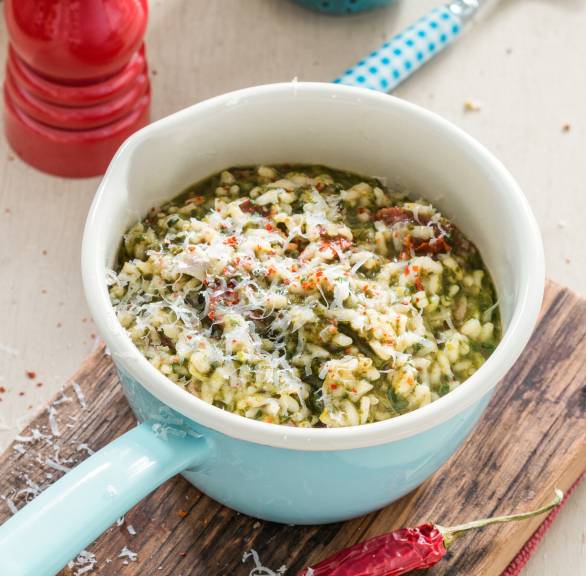 Grünkohlrisotto mit Pancetta, getrockneten Tomaten und Parmesan in einem kleinen Stieltopf auf einem Tisch
