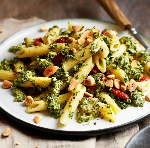 Nudelpfanne mit Grünkohl, grünem Pesto, getrockneten Tomaten und Mandeln angerichtet auf einem Teller