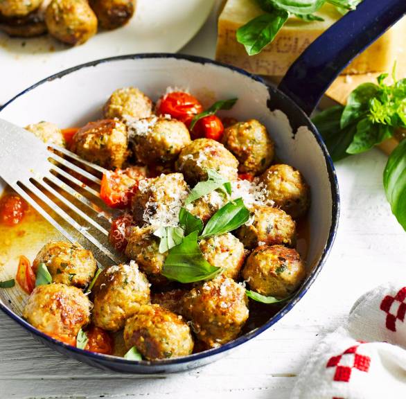 Pfanne mit Hackbällchen und Kirschtomaten garniert mit Basilikum auf einem Tisch