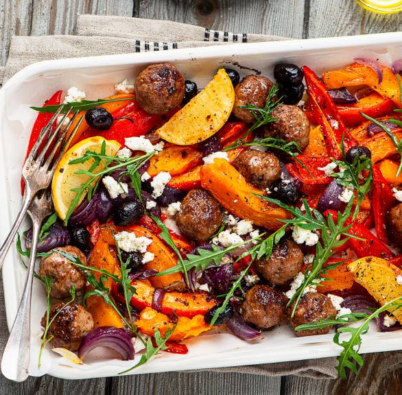 Hackfleischbällchen und Gemüse auf einem Backblech getoppt von Feta, Rucola und Zitronenspalten