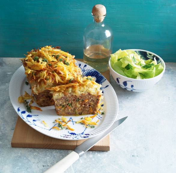 Hackbraten mit Kartoffelhaube angeschnitten auf einer Platte, daneben eine Schale mit grünem Salat und Olivenöl
