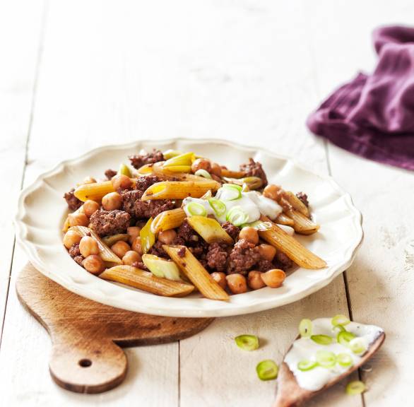 Nudel-Hackfleisch-Pfanne angerichtet auf einem tiefen Teller, getoppt mit saurer Sahne und Frühlingszwiebelringen