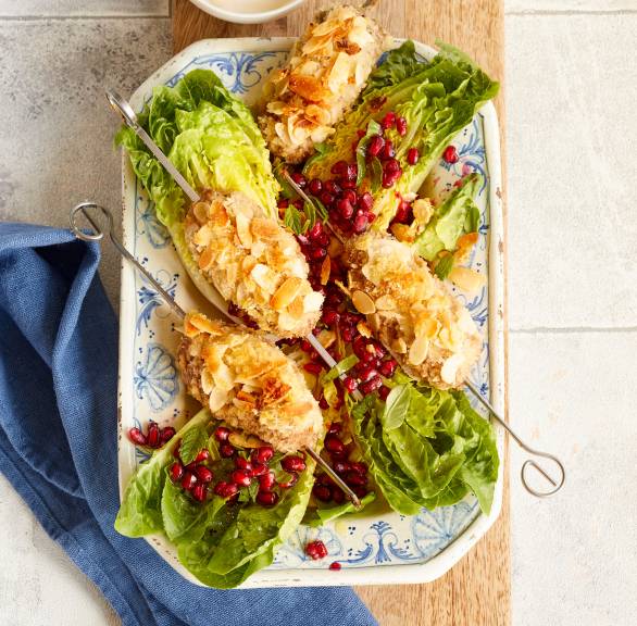 Vier gebackene Low-Carb-Hackspieße mit Mandel-Panko-Kruste angerichtet auf einer Platte mit Granatapfel-Minz-Salat