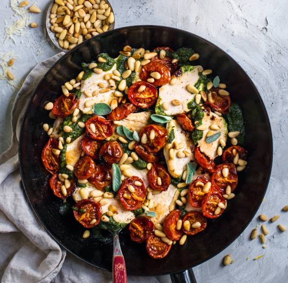 Hähnchen-Scaloppine in einer Pfanne mit Ofentomaten und Salbei-Pesto bestreut mit gerösteten Pinienkernen