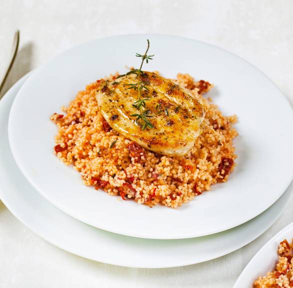 Gebratenes Hähnchen-Minutenschnitzel auf Tomaten-Couscous angerichtet auf einem tiefen Teller