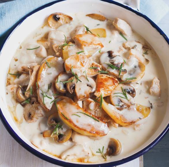 Hähnchenragout in Sahnesauce in einer Pfanne mit Champignons und Apfelspalten