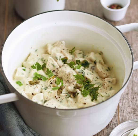 Hähnchenragout in Sahnesauce in einem Topf auf einem Holztisch
