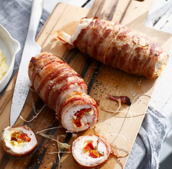 Zwei angeschnittene Hähnchenrouladen im Pancettamantel auf einem Holzbrett