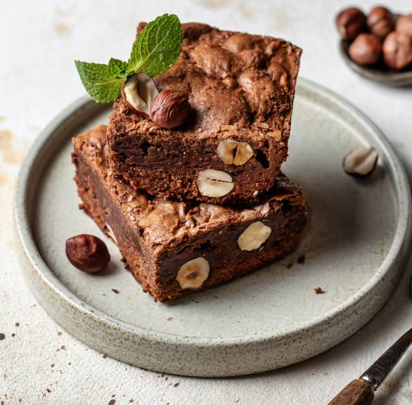 Zwei Stücke Brownies mit Haselnüssen angerichtet auf einem Kuchenteller garniert mit frischer Minze
