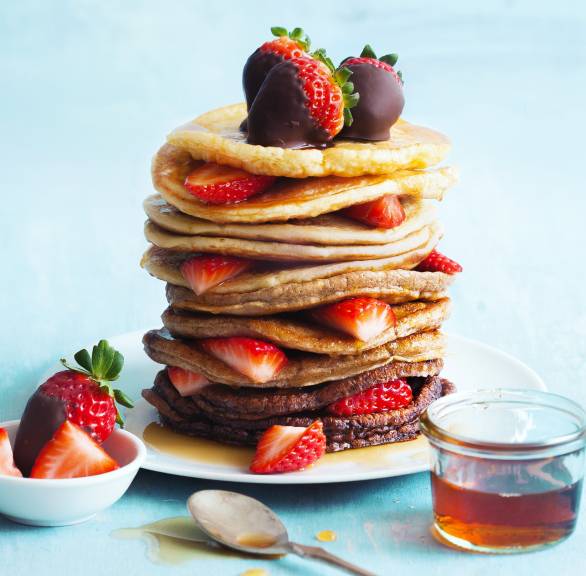 Helle und dunkle Pfannkuchen abwechselnd aufgetürmt auf einem Teller, daneben Erdbeeren mit Schokomantel