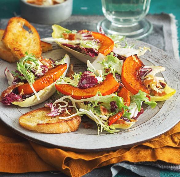 Herbstlicher Salat angerichtet mit Kürbisspalten und Ciabatta auf einem Teller