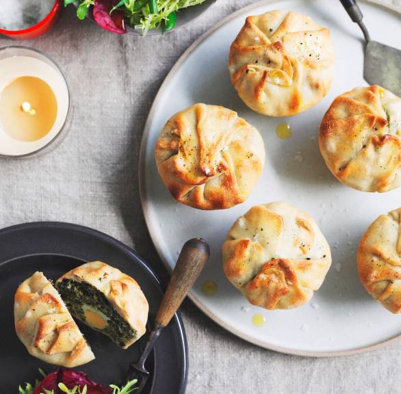 Herzhafte Mini-Osterkuchen auf einem Teller, daneben eines aufgeschnitten mit Füllung aus Spinat, Ricotta und Ei