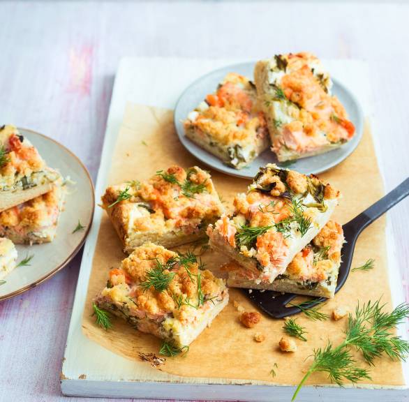 Stücke vom Lachskuchen gestapelt auf einem Holzbrett getoppt mit Dillzweigen