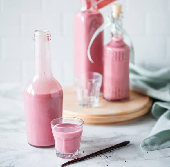 Selbst gemachter Himbeer-Eierlikör in zwei Flaschen sowie Pinneken auf einem Tisch