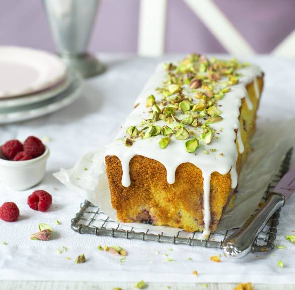 Selbstgebackener Mascarpone-Kastenkuchen mit Himbeeren getoppt von Zitronenguss und Pistazien auf einem Kuchengitter