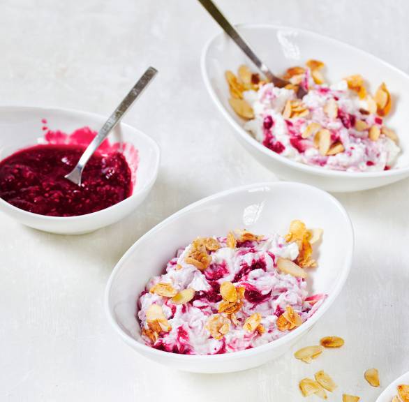 Himbeer-Ricotta-Creme in mehreren Dessertschälchen getoppt von karamellisierten Mandelblättchen auf einem Tisch