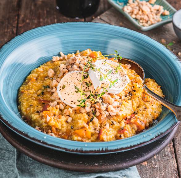 Hirsotto Risotto aus Hirse mit Karotten und Ziegenkäse angrichtet auf einem Teller getoppt von Walnüssen