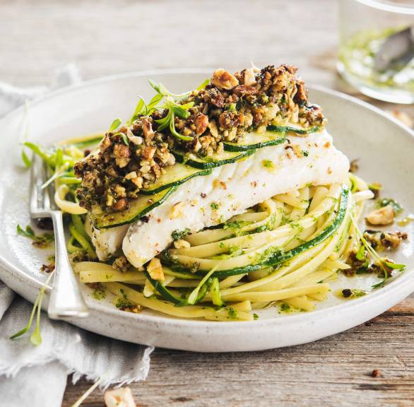 Kabeljau aus dem Ofen mit Nusskruste angerichtet auf einem Bett aus Linguine und Zucchininudeln