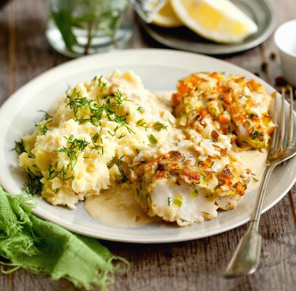 Gebratener, panierter Kabeljau auf einem Teller getoppt mit Estragonsauce, daneben Zitronenviertel