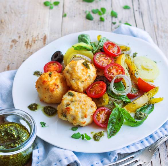 Fischbällchen auf einem Teller, daneben Kartoffelsalat getoppt mit Pesto und frischem Basilikum