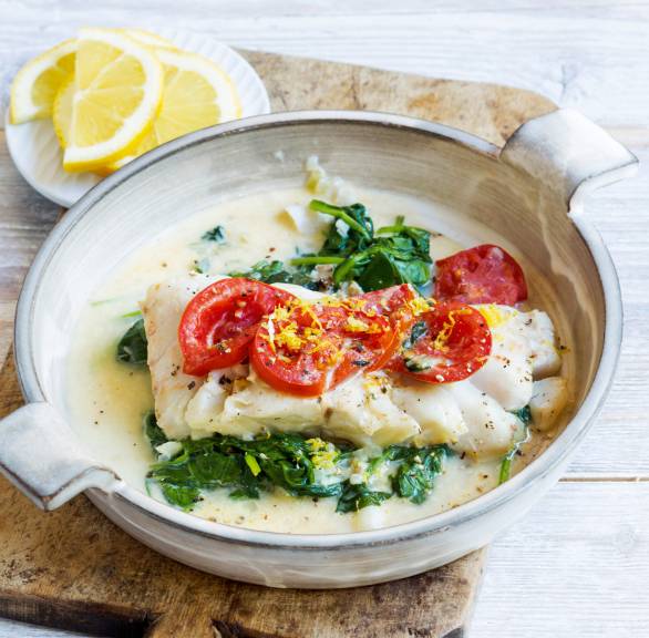 Kabeljau auf Rahmsppinat getoppt von Tomaten und geriebener Zitronenschale in einer Pfanne