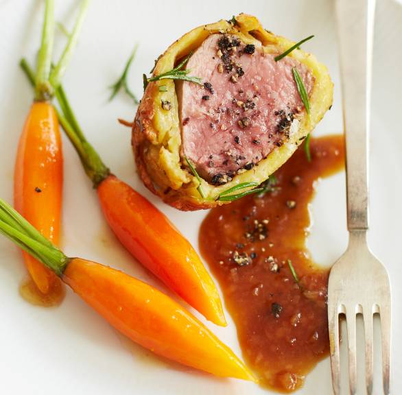 Ein Stück Kalbsfilet im Kartoffelmantel angerichtet mit Honig-Karotten und dunkler Sauce auf einem Teller