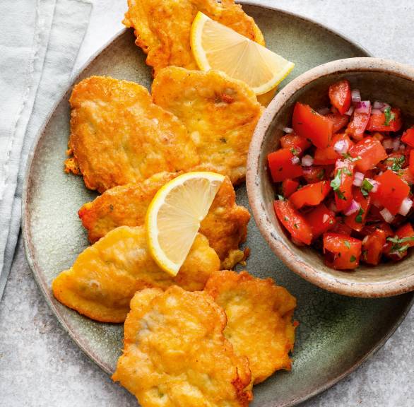 Mehrere Kalbsschnitzel in Parmesanpanade auf einem Teller mit einer Schale mit Tomatensalat