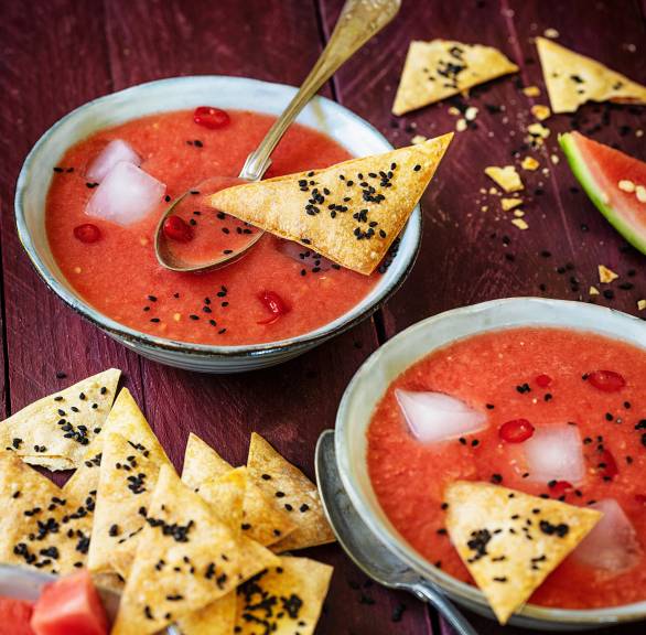 Tomatensuppe mit Eiswürfeln in zwei Schalen getoppt mit dreieckigen Crackern auf einem Tisch