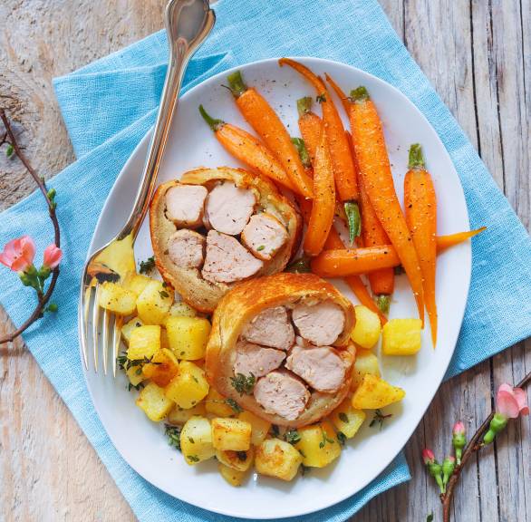 Gebackenes Kaninchenfilet im Brotmantel angerichtet auf einem Teller mit Thymiankartoffeln und ganzen, glasierten Karotten