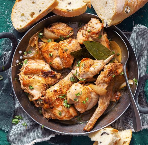 Geschmortes Kaninchen in einer Auflaufform, daneben selbstgebackenes Oliven-Ciabatta