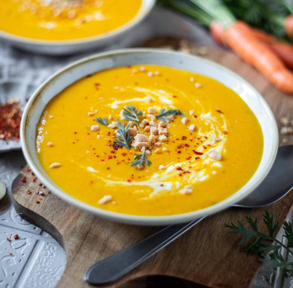 Karotten-Cremesuppe in zwei tiefen Tellern auf einem Tisch, daneben Bundmöhren