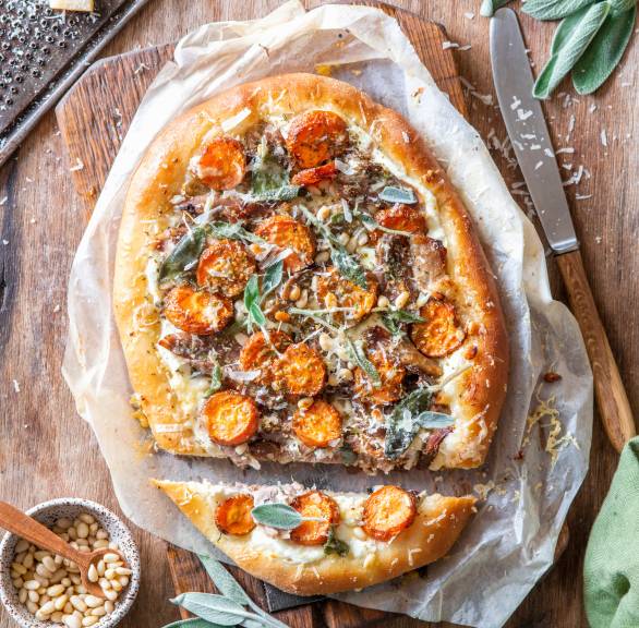 Ovale Pizza mit Entenbrust, Karotten und Pilzen belegt angeschnitten und mit Pinienkernen daneben