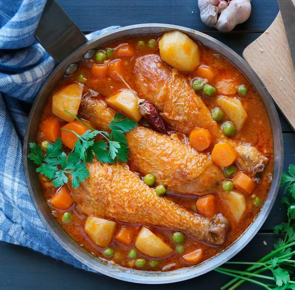 Kartoffeleintopf mit Hähnchen, Erbsen, Gemüse und Speck von oben in einem Topf, daneben angeschnittenes Baguette auf einem Holzbrett
