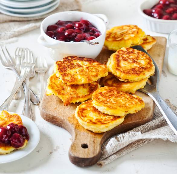 Mehrere gebratene Kartoffelküchlein auf einem Holzbrett, daneben mit Glühwein-Kirschen-Sauce in einer Schale