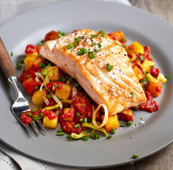 Kartoffelpfanne mit Gemüse auf einem Teller, darauf ein Stück gebratener Lachs