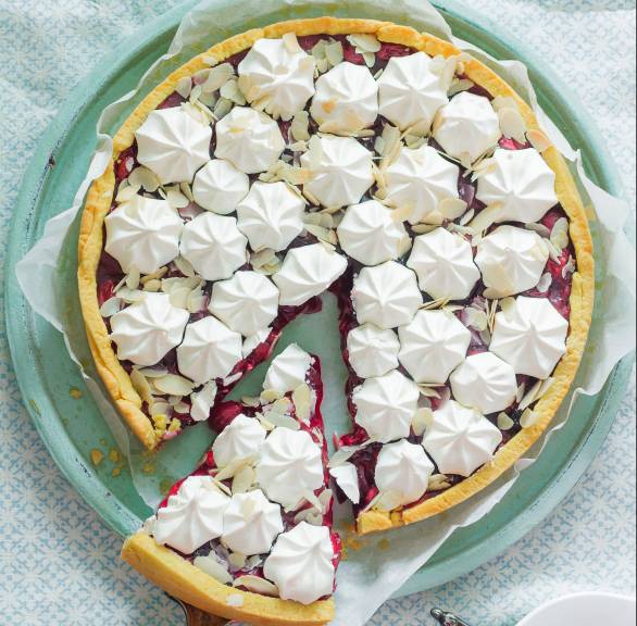 Runder Kirschkuchen mit Amaretto und Baisertüpfelchen angeschnitten auf einer Kuchenplatte auf einem Holztisch von oben