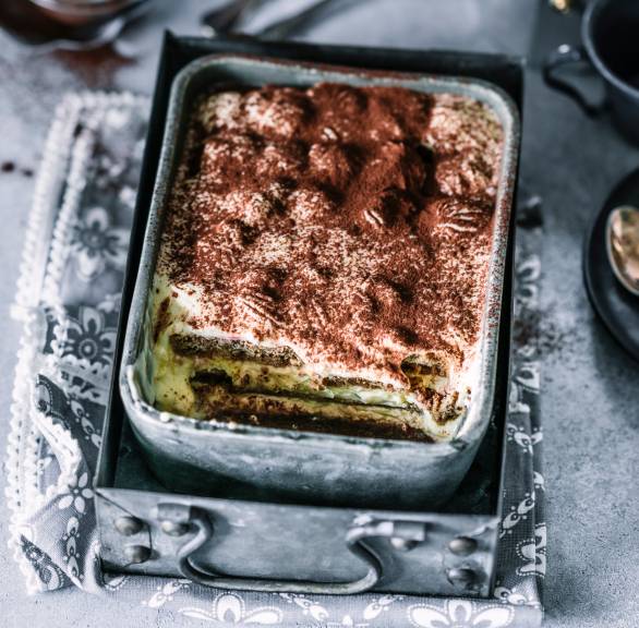 Tiramisu in einer metallenen Auflaufform angeschnitten auf einem Tisch