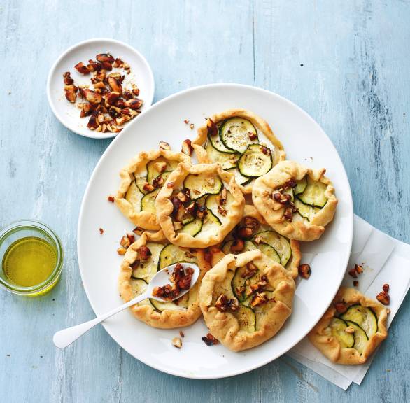 Sechs selbst gebackene Galettes belegt mit Zucchini und Ricotta getoppt von Gewürzmandeln auf einer Vorspeisenplatte