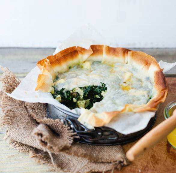 Selbstgebackener, angeschnittener Spinat-Feta-Kuchen mit Filoteig und Datteln in einer kleinen Springform auf einem Tisch