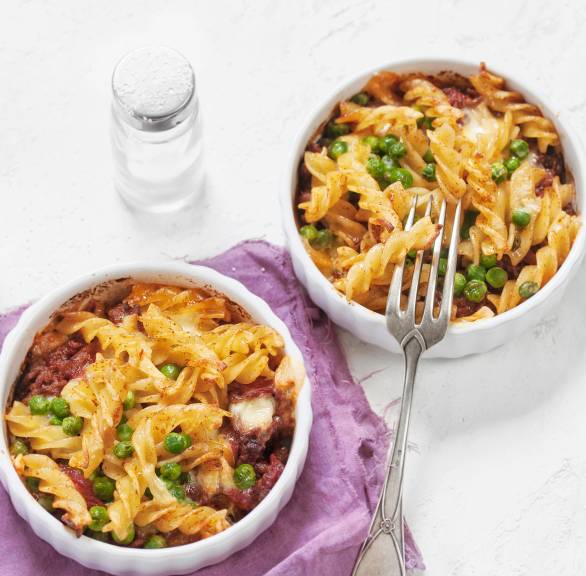 Fusilli mit Hackfleischragout und Erbsen in zwei kleinen runden Auflaufformen auf einem Tisch