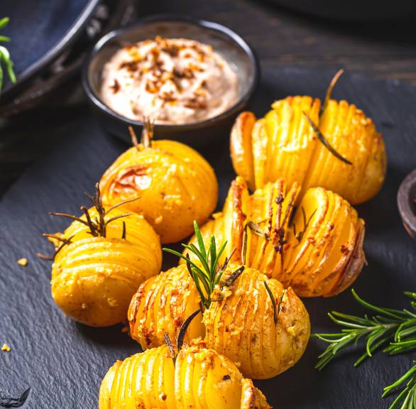 Fächerkartoffeln auf einem Schieferteller mit Rosmarin gespickt, daneben Schafskäse-Tomaten-Dip