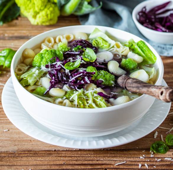 Minestrone mit verschiedenen Kohlsorten, Nudeln und Romanesco in einem Topf und einem Suppenteller auf einem Tisch