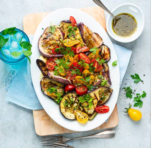 Grillgemüse auf einem ovalen Teller, daneben eine Schüssel mit Marinade