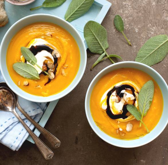 Kürbis-Apfelsuppe in zwei Suppenschalen auf einem Tisch, daneben baguette