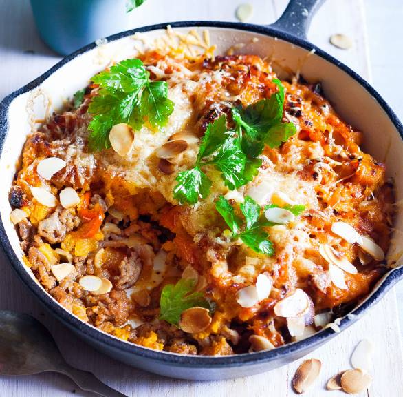 Kürbis-Hackauflauf in einer Pfanne auf einem Holztisch, daneben Basilikum