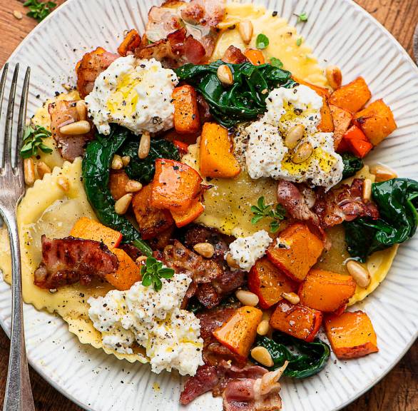 Kürbisravioli auf einem Teller getoppt mit Spinat, Pancetta und Ricottaflocken